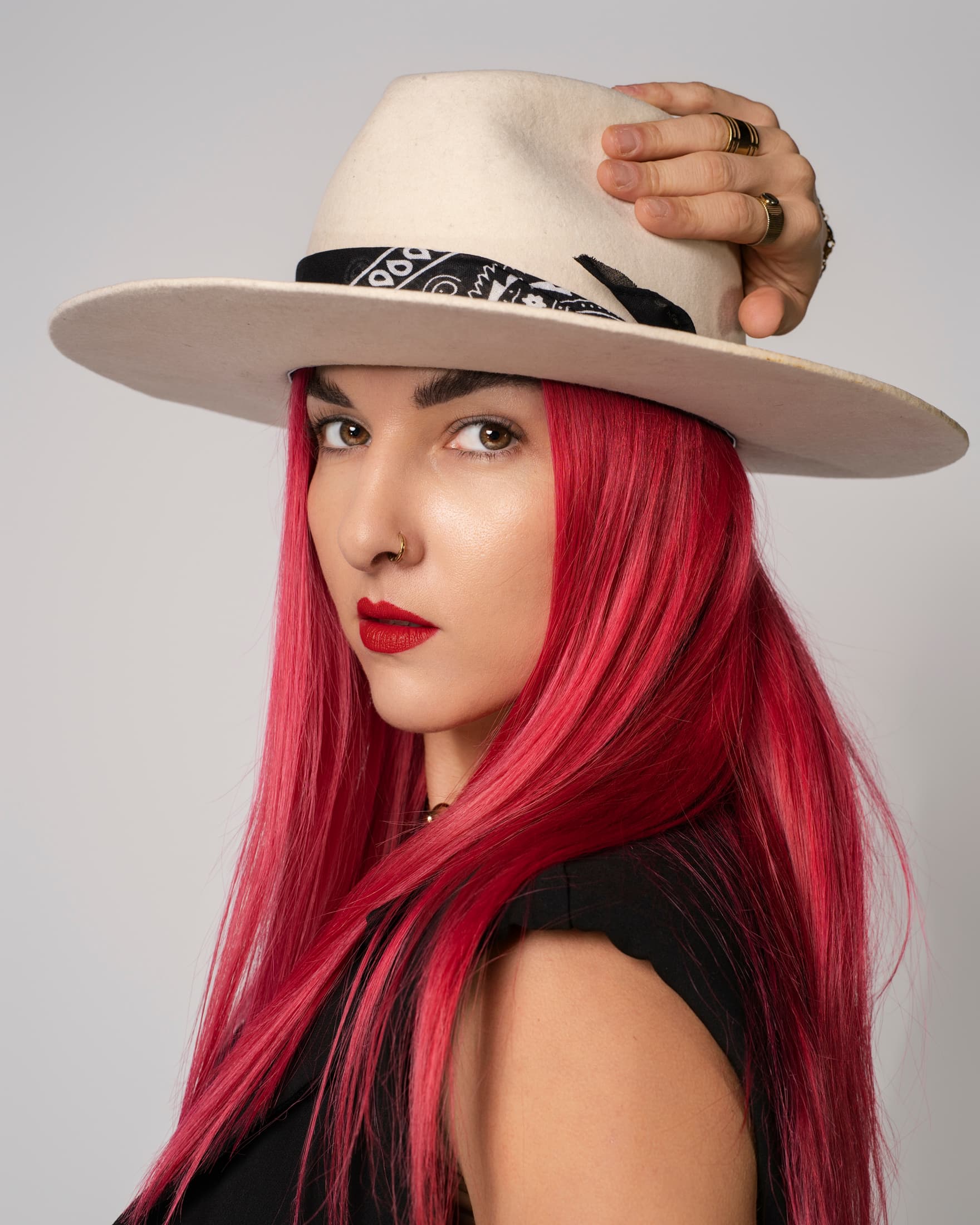 Donna con capelli rosa acceso, cappello bianco a tesa larga e rossetto rosso intenso.