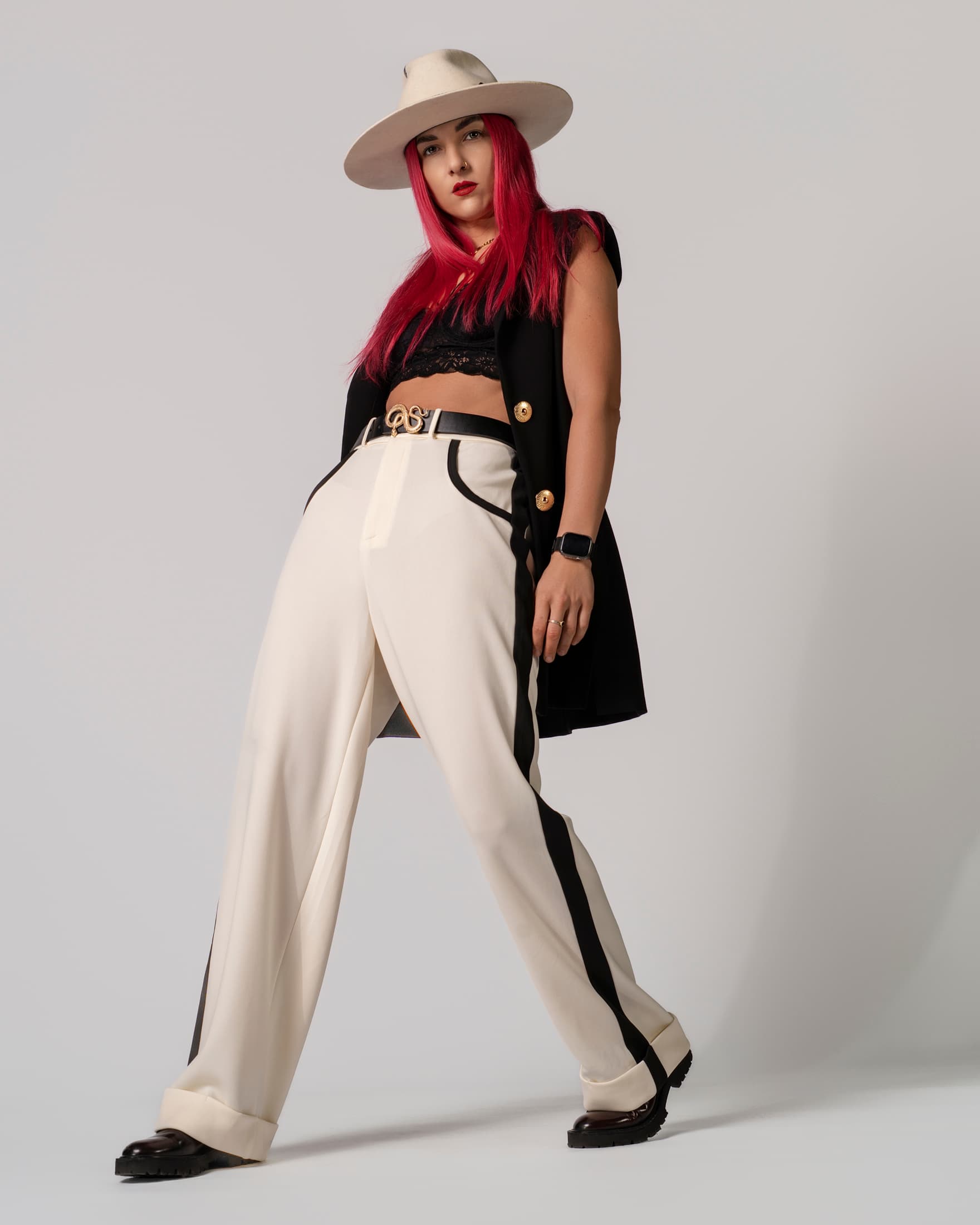 Donna con capelli rosa, cappello panna, gilet nero e pantaloni bianchi con strisce nere.
