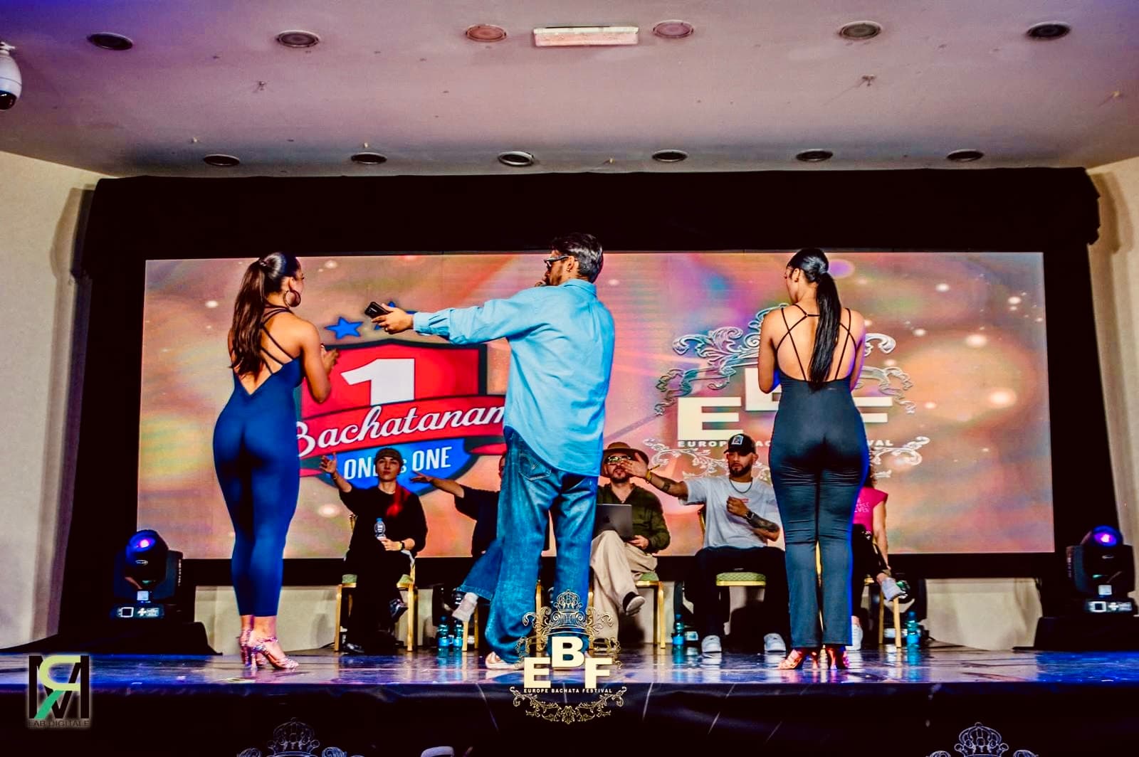 Due donne in tuta e un uomo su un palco per una competizione di bachata.