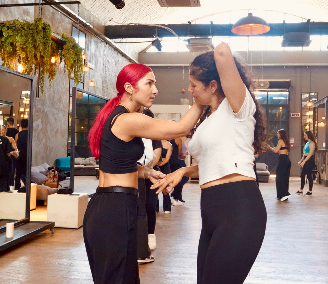 Due donne ballano in uno studio luminoso, una con capelli rossi e l'altra ricci.
